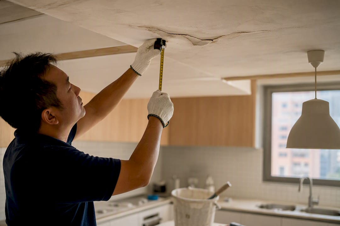 Contractor inspecting bulging plaster ceiling crack