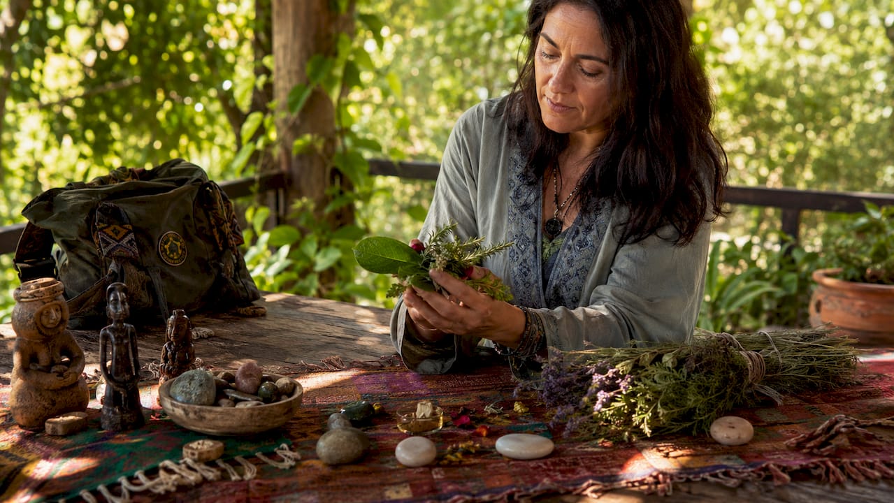 Hands holding medicinal leaf and ritual herbs on wooden table