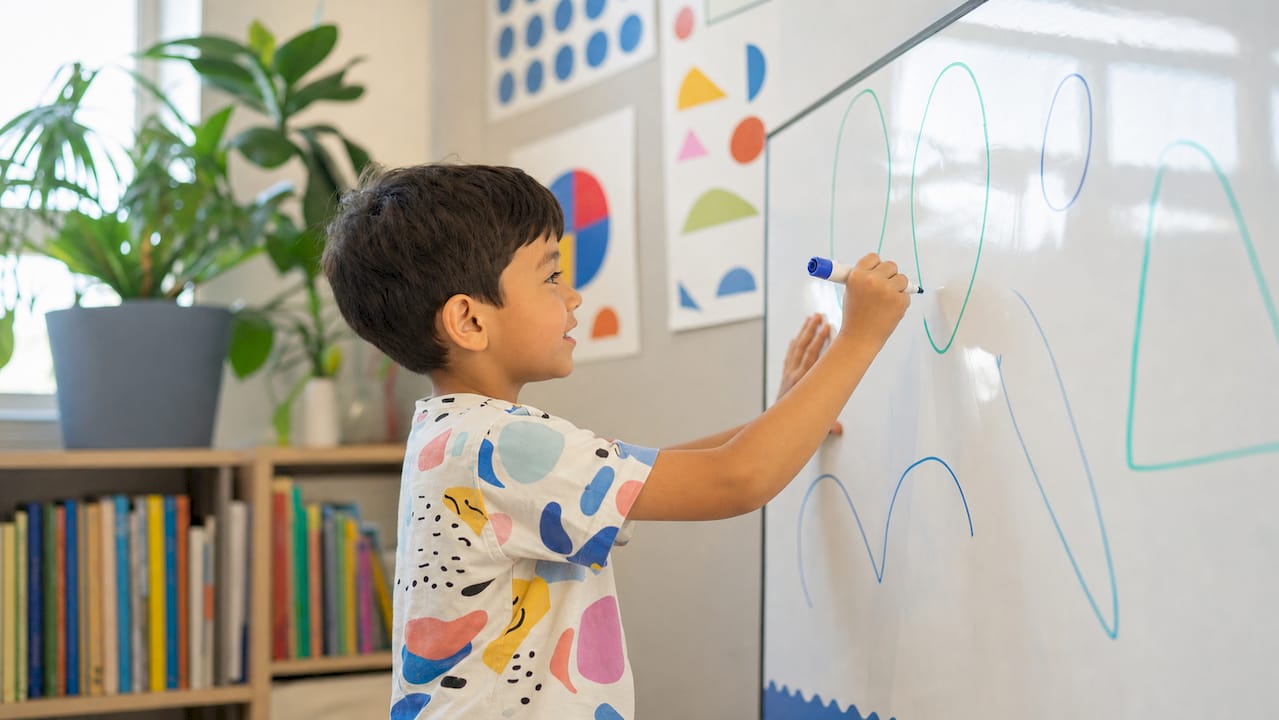 Child marking letters on whiteboard chart