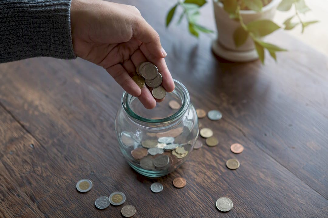 Hand pouring coins into savings jar