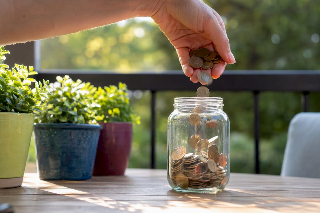 Hand pouring coins into 401(k) match savings jar