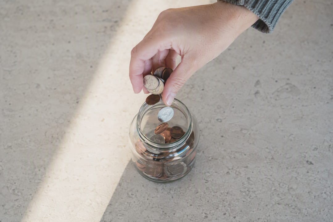 Hand pouring coins into glass savings jar