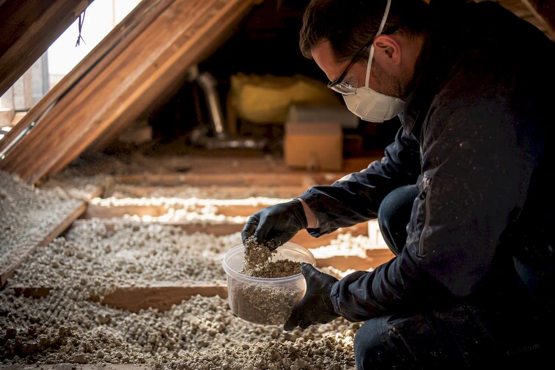 Hands collecting vermiculite sample in attic