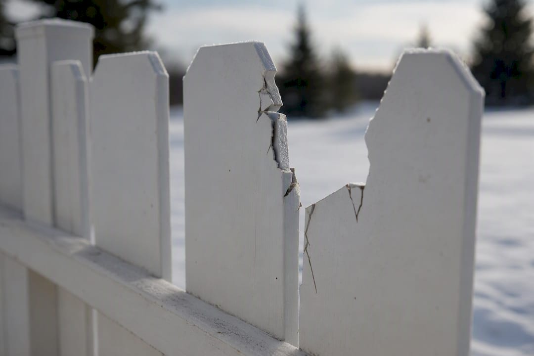 Cracked vinyl fence panel in snowy setting