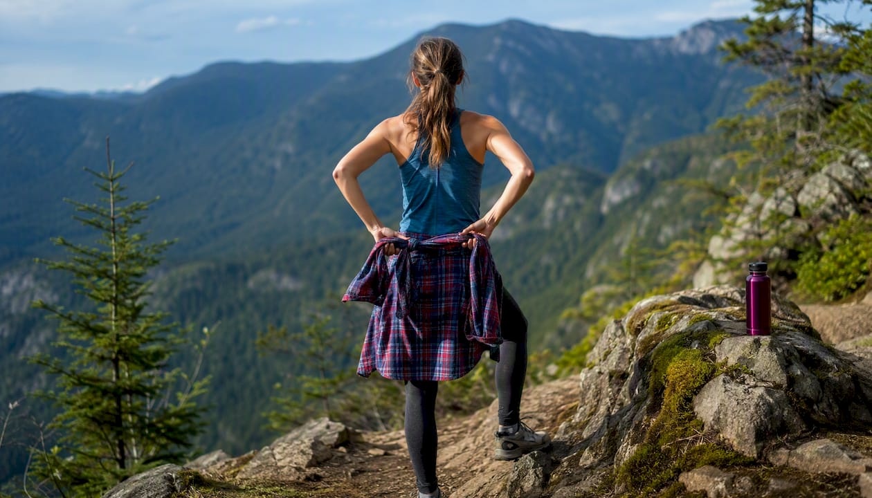 Person tying flannel shirt at waist for hiking outfit