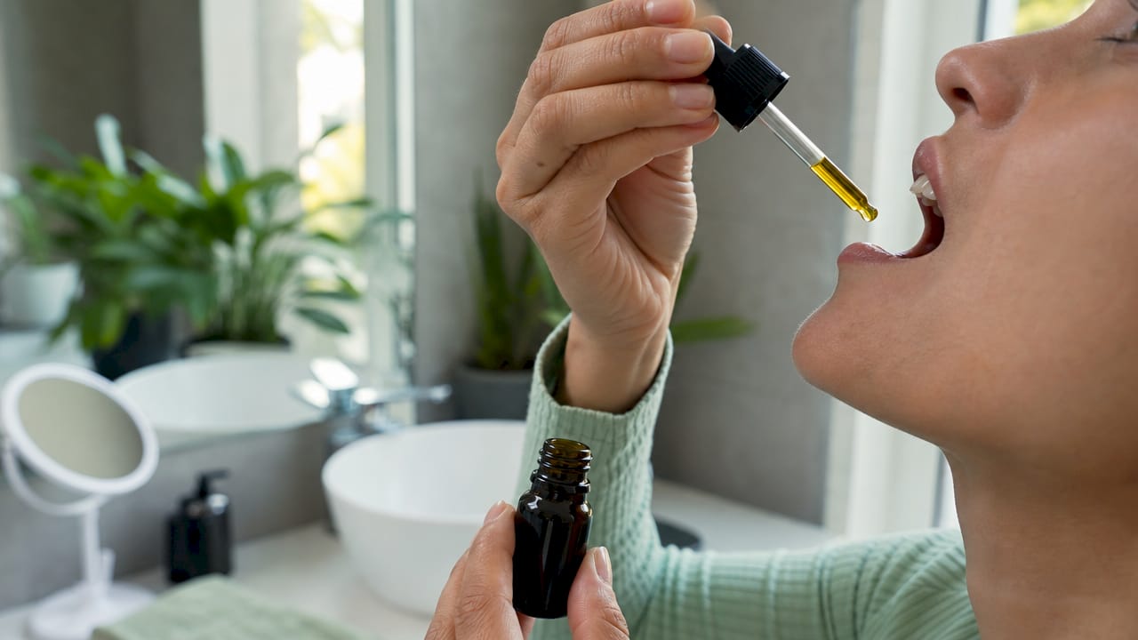Gros plan sur des mains qui déposent quelques gouttes d’huile de CBD sous la langue.