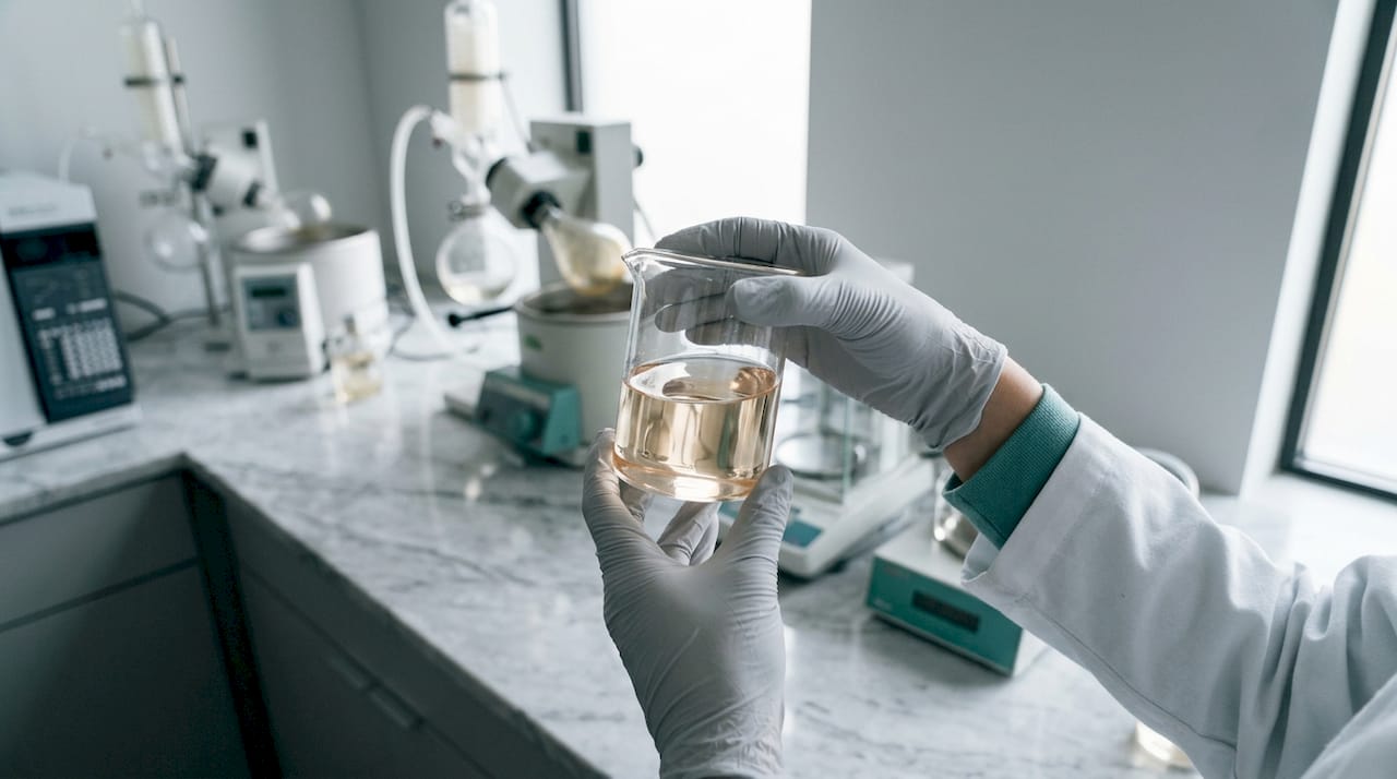 Unas manos manipulan un frasco lleno de un producto químico en un laboratorio.