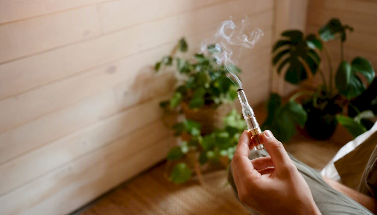Une main tient une cigarette électronique d’où s’échappe une fine volute de vapeur.