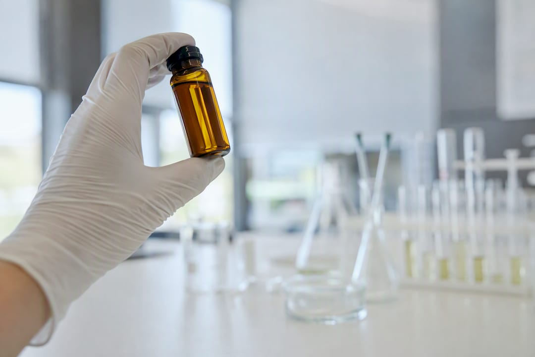 Une main gantée tient un flacon d’huile de chanvre dans un laboratoire.