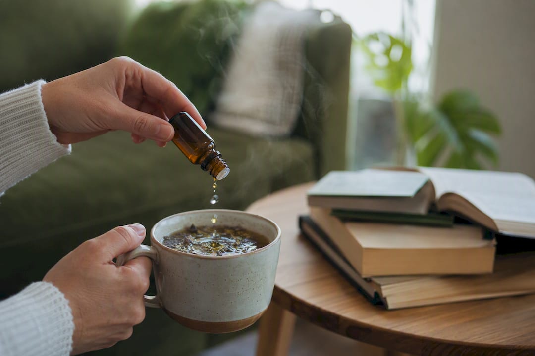 Main tenant un compte-gouttes d'huile de CBD au-dessus d'une tasse de tisane