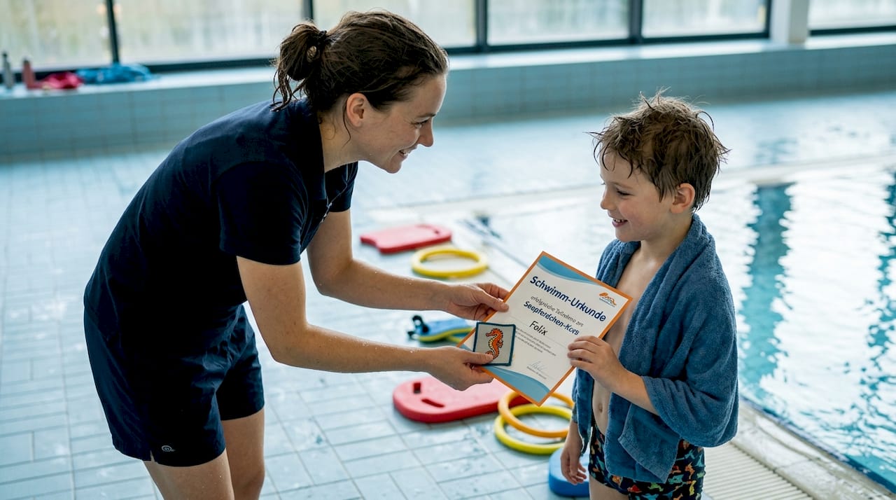 The swimming instructor proudly presents a child with a certificate at the poolside.
