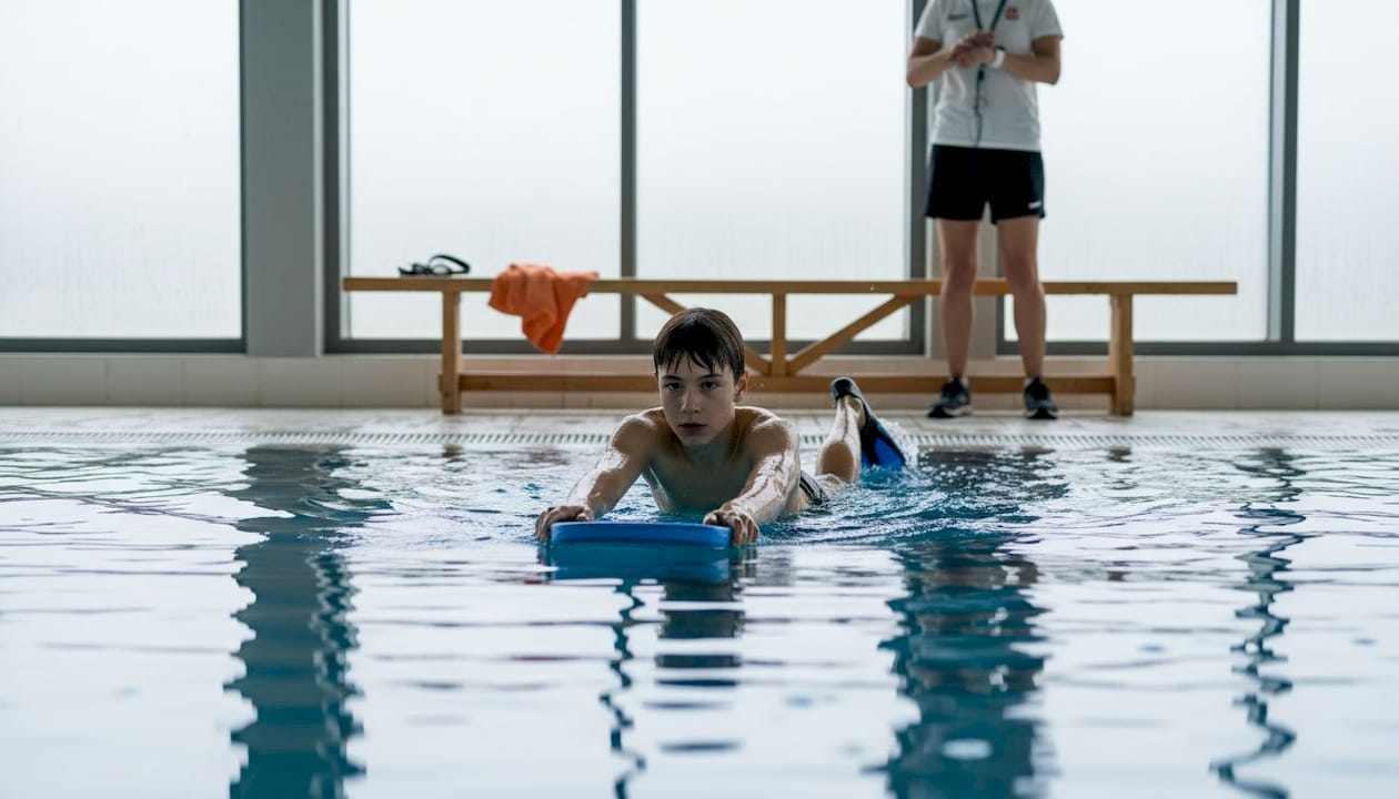 Experienced swimmer training with a kickboard under the guidance of a coach.