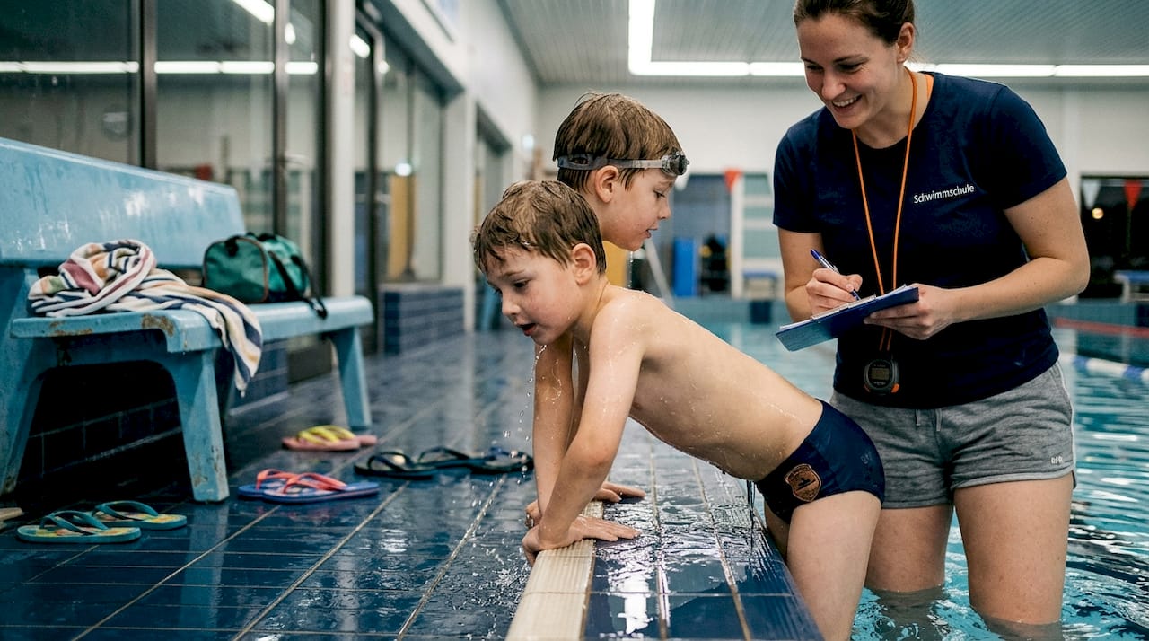 Kind nach bestandener Bronze-Schwimmprüfung mit dem Schwimmlehrer