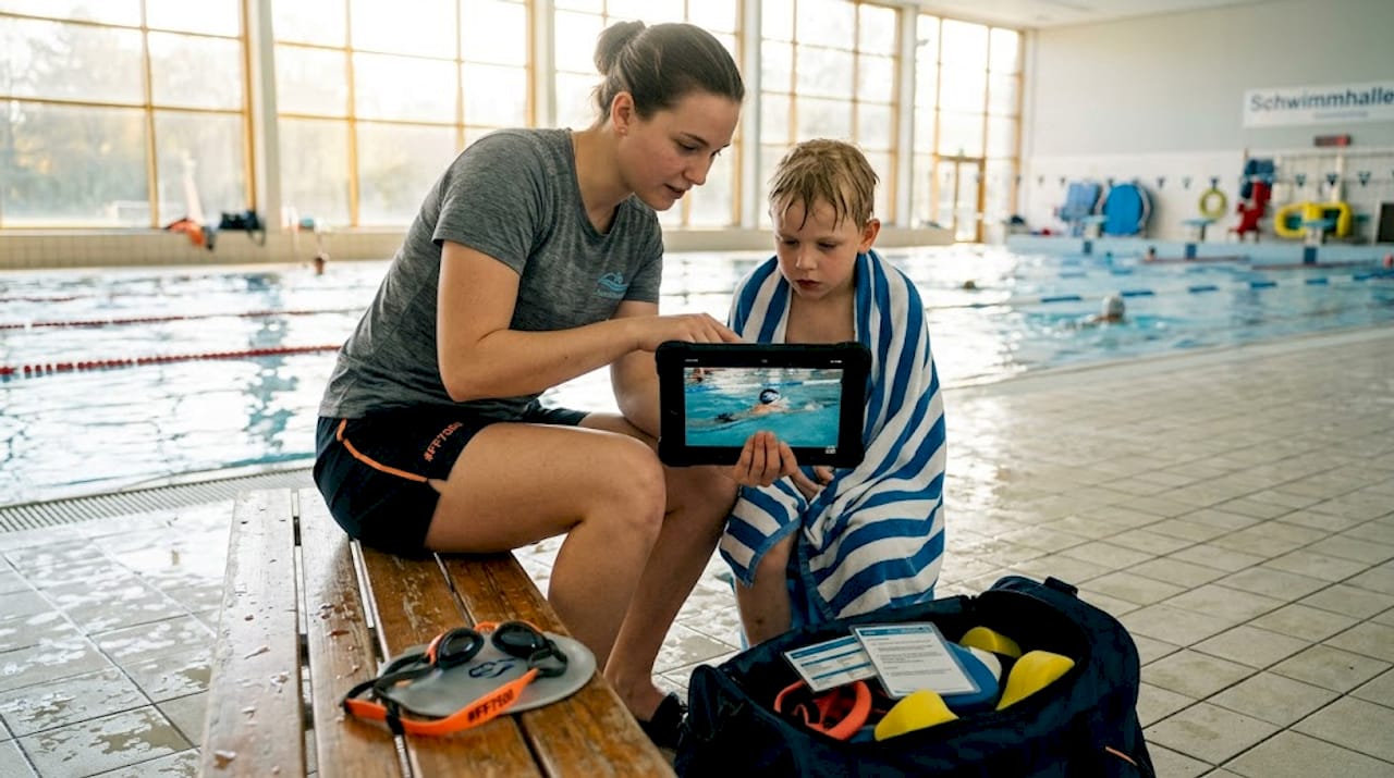 Am Beckenrand erklärt die Trainerin dem Kind mithilfe einer Videoanalyse, wie es seine Schwimmtechnik verbessern kann.