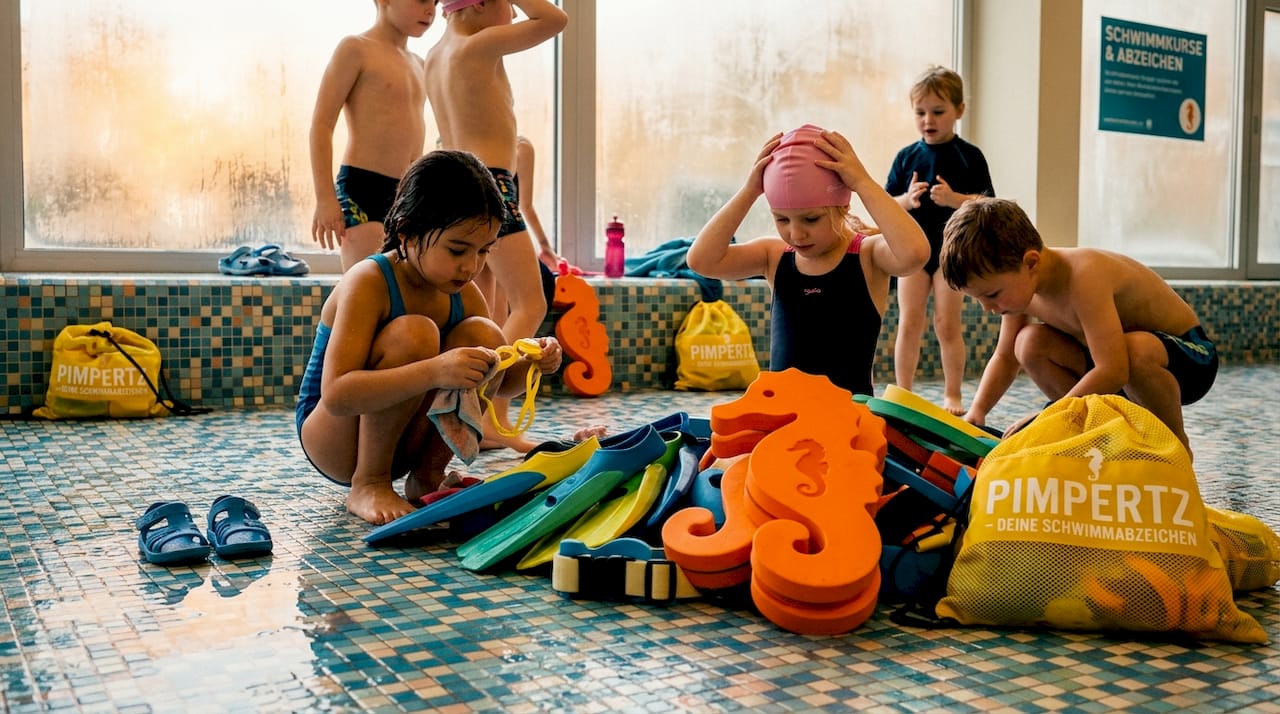 Grundschulkinder sortieren buntes Schwimmzubehör, das sie zum Mitmachen motiviert.