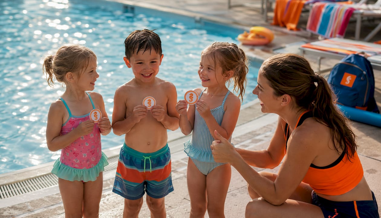 Am Beckenrand üben Kinder gemeinsam mit ihrem Trainer für ihre Schwimmabzeichen.