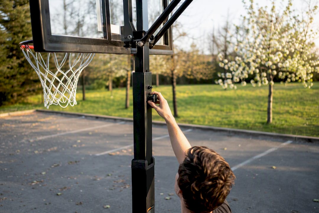 Hände stellen die Höhe eines tragbaren Basketballkorbs ein