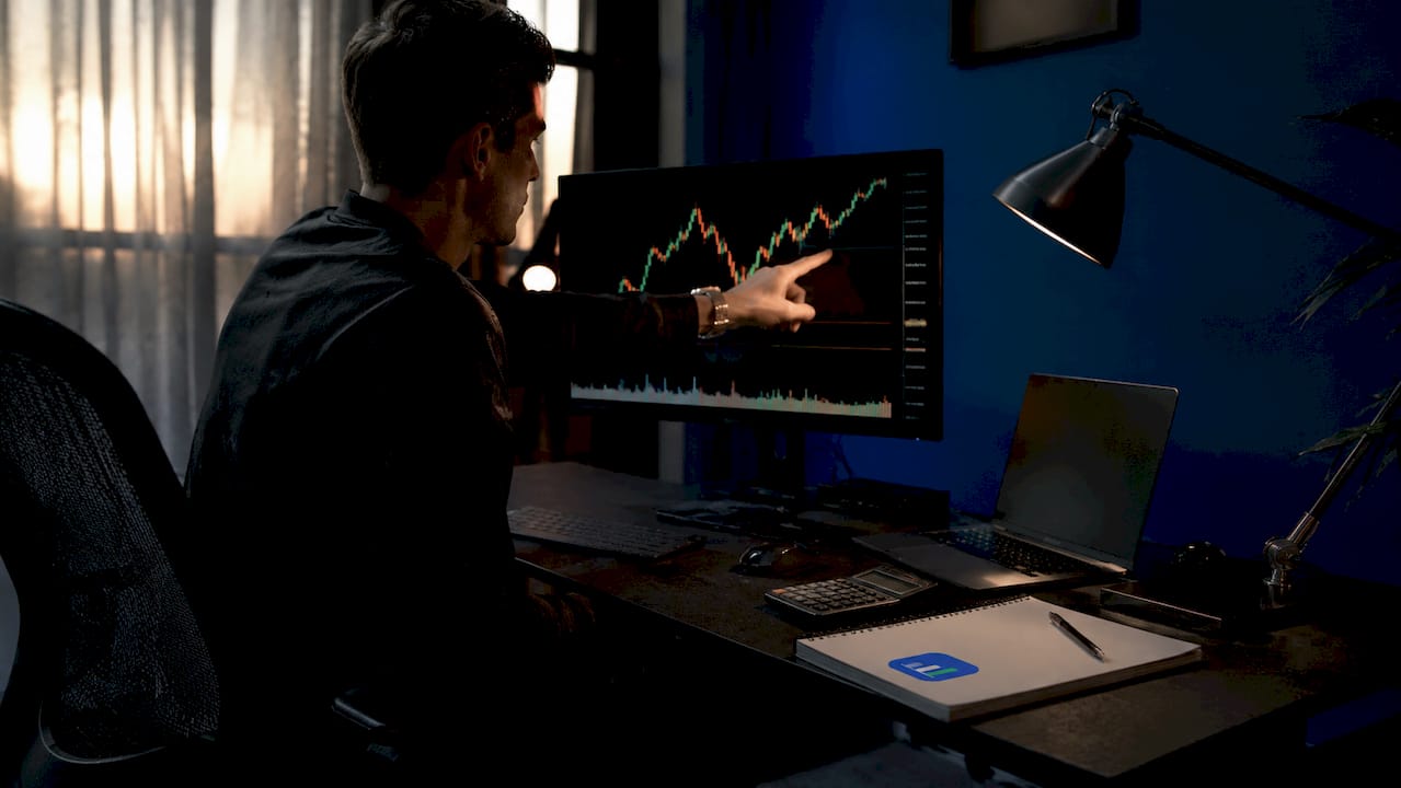 Trader pointing at dual-monitor trading charts