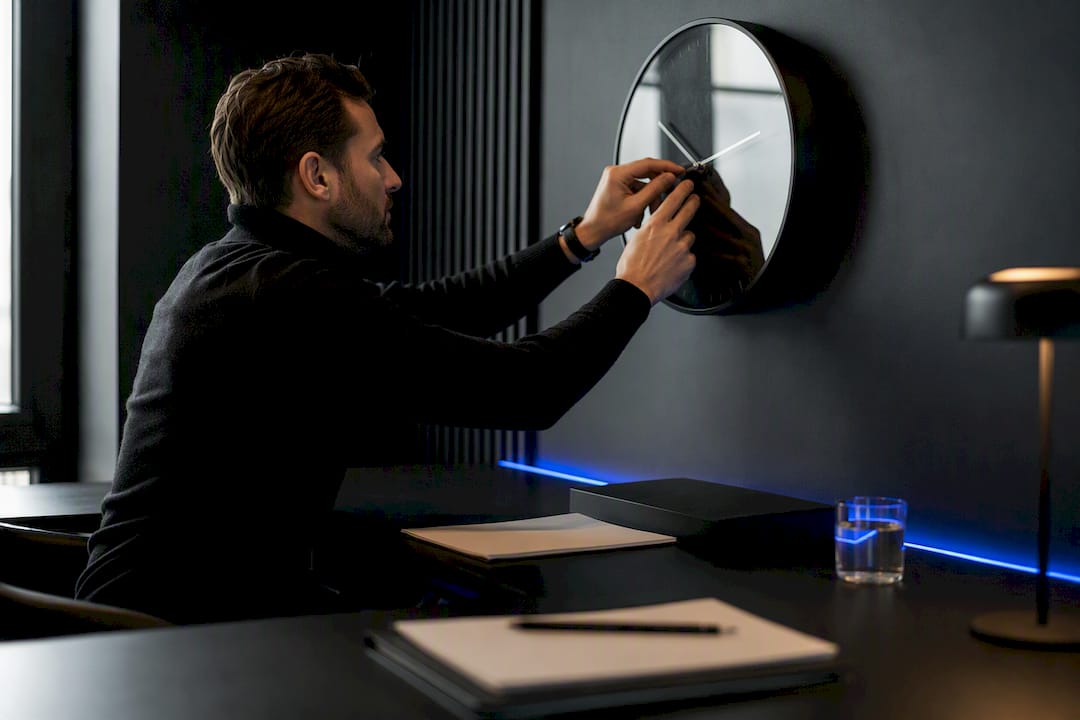 Trader adjusting analog desk clock on dark desk