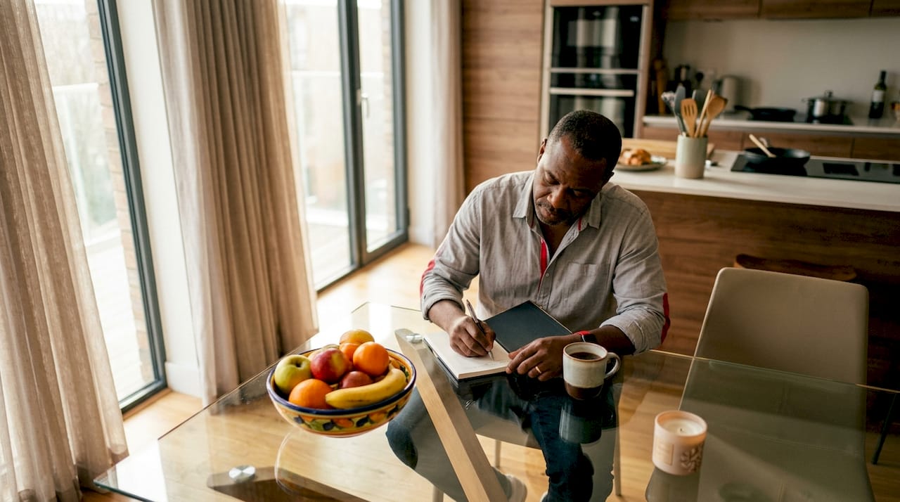 Man noting gift recipient preferences at kitchen table