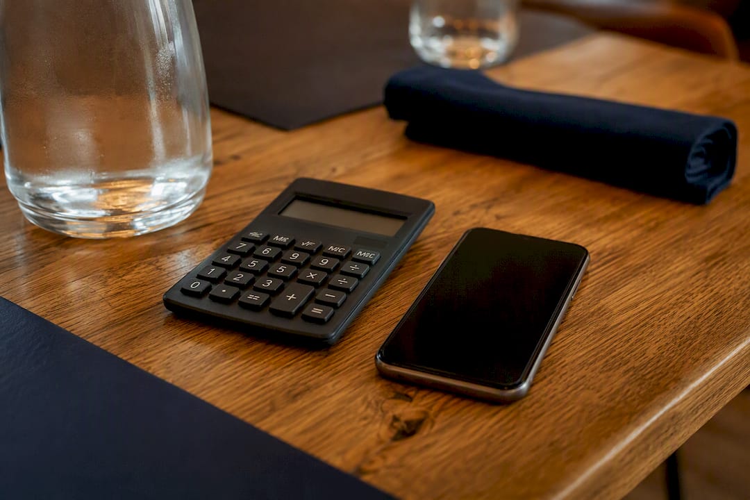 Een rekenmachine en een smartphone liggen naast elkaar op een houten tafel.