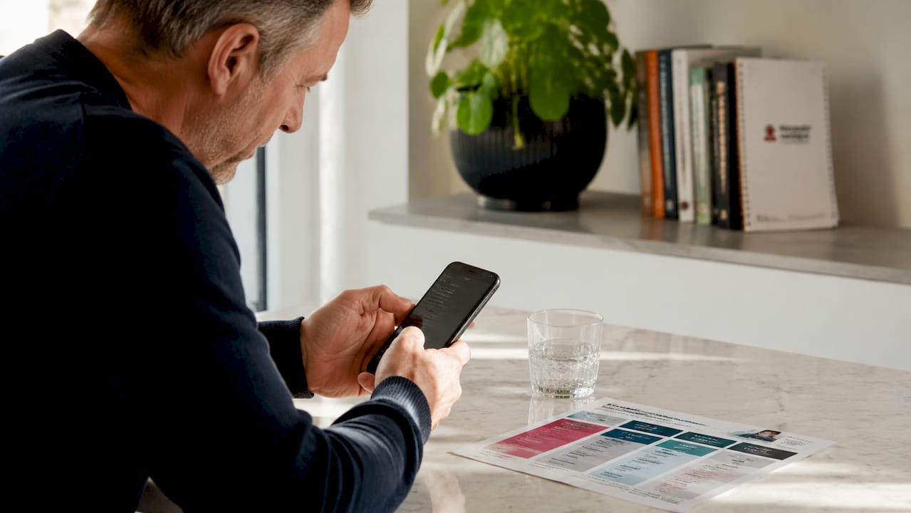 Een man zit thuis aan de keukentafel en vergelijkt verschillende mobiele abonnementen.