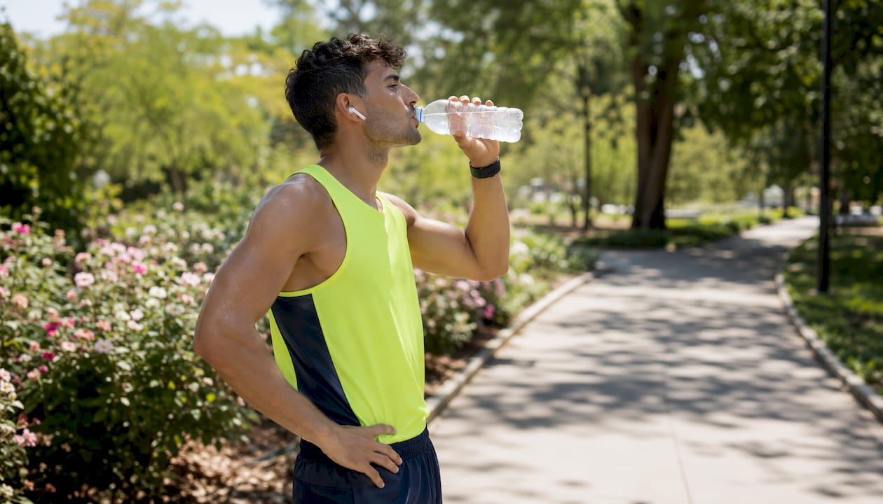 Jogger drinking sports drink outdoors at dawn