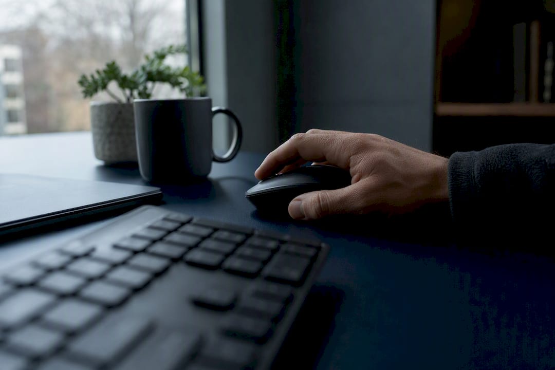 Hand clicking mouse beside dark laptop