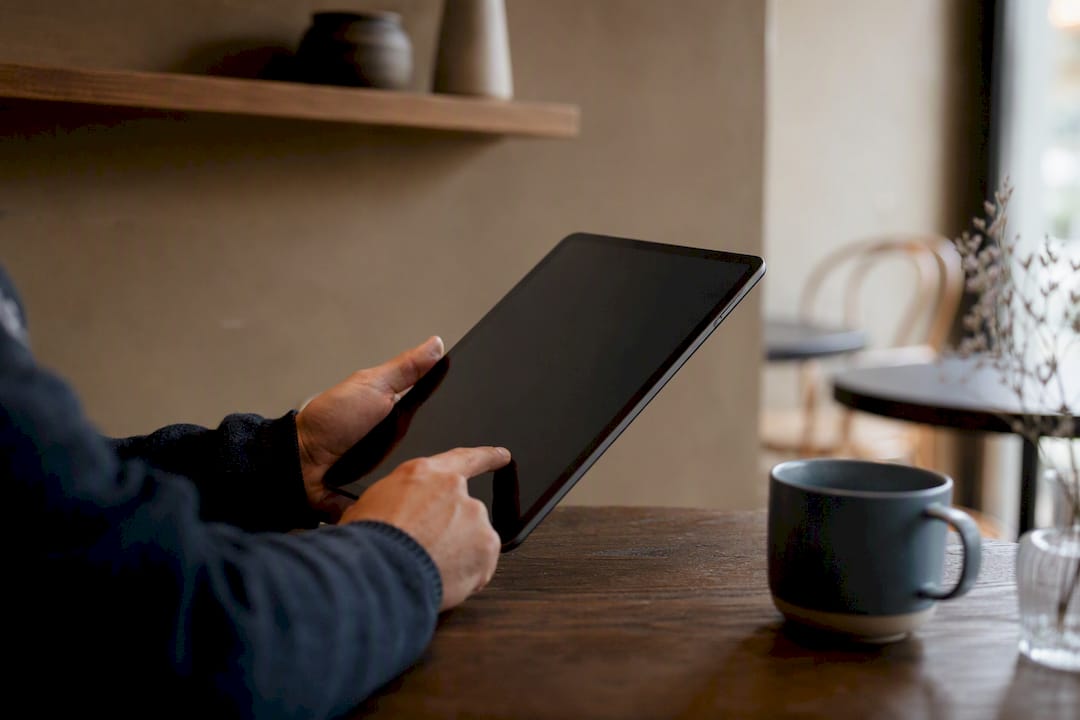 Hands arranging items near tablet and mug