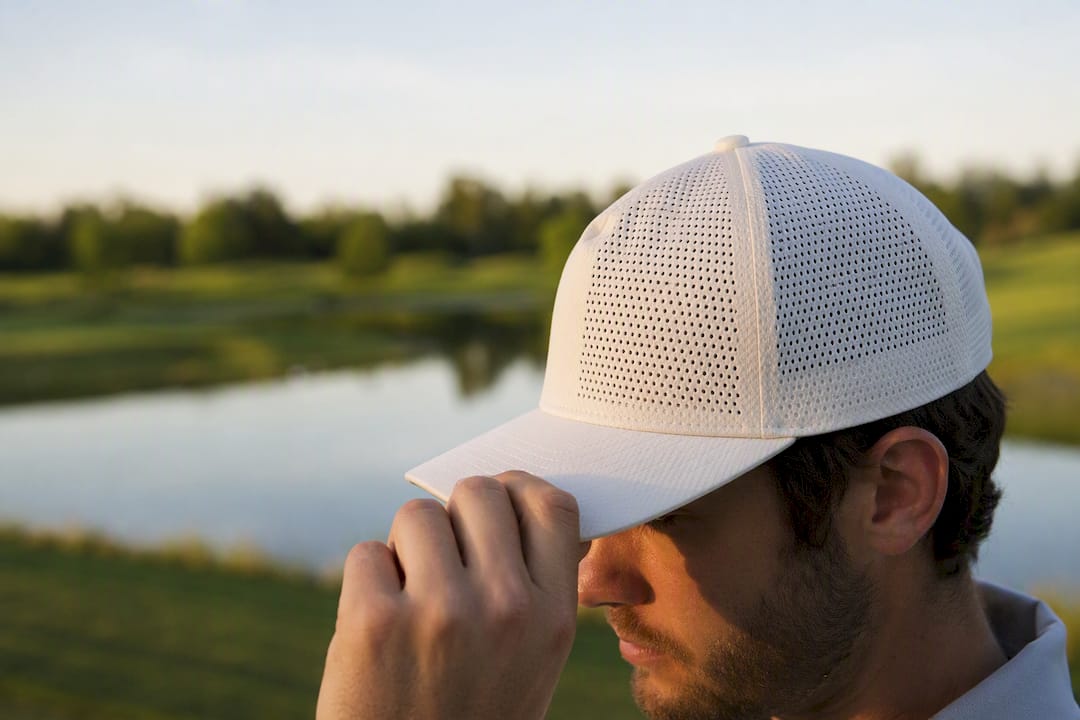Golfer adjusting perforated breathable golf hat on course