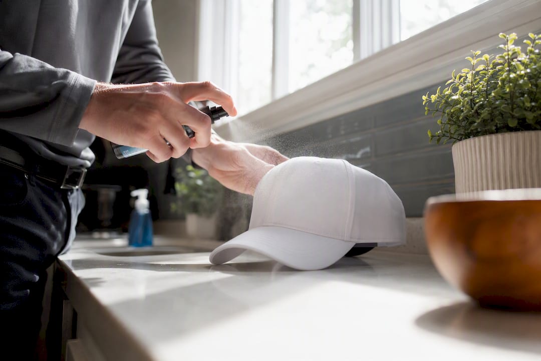 Hands spraying protectant on new golf hat indoors