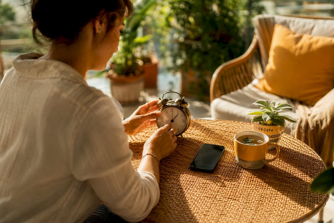 Hands adjusting wristwatch near phone and mug