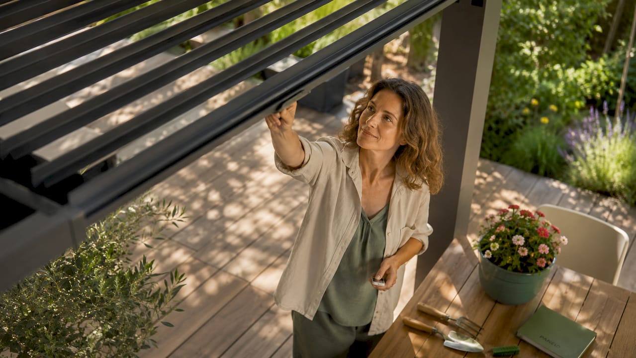 Eine Frau stellt die Lamellen ihrer bioklimatischen Pergola individuell ein.
