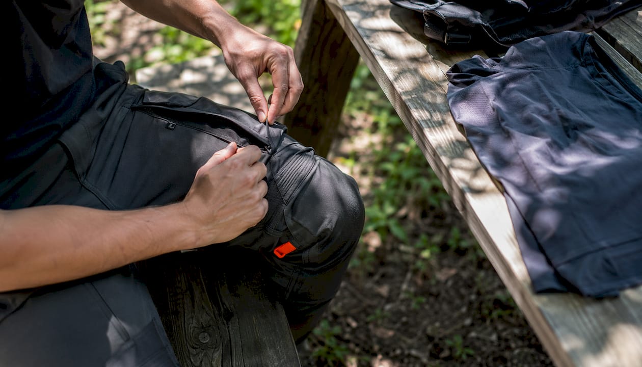 Hands adjusting reinforced tactical travel pants indoors