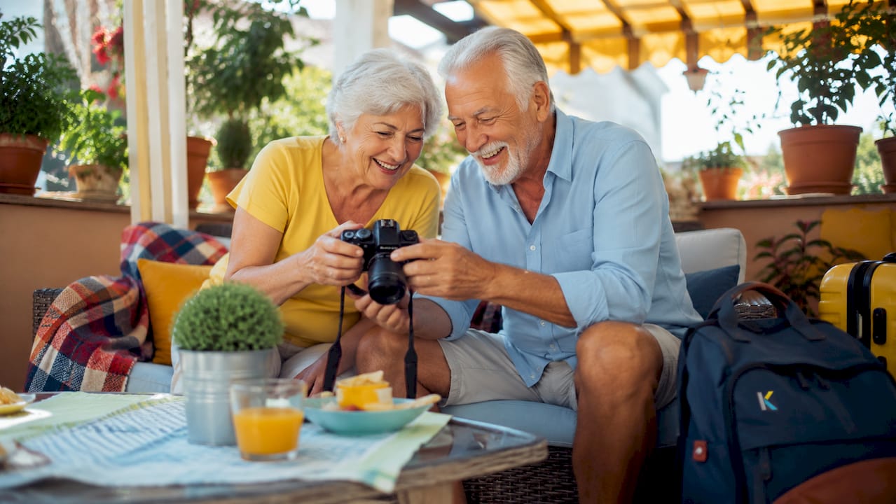 Elderly couple reviewing vacation videos on camera outdoors