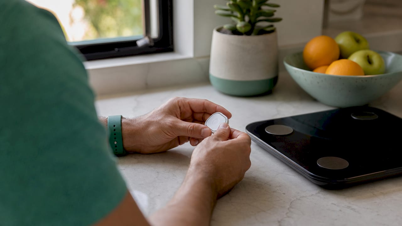 Hands holding glucose monitor and smart scale on desk