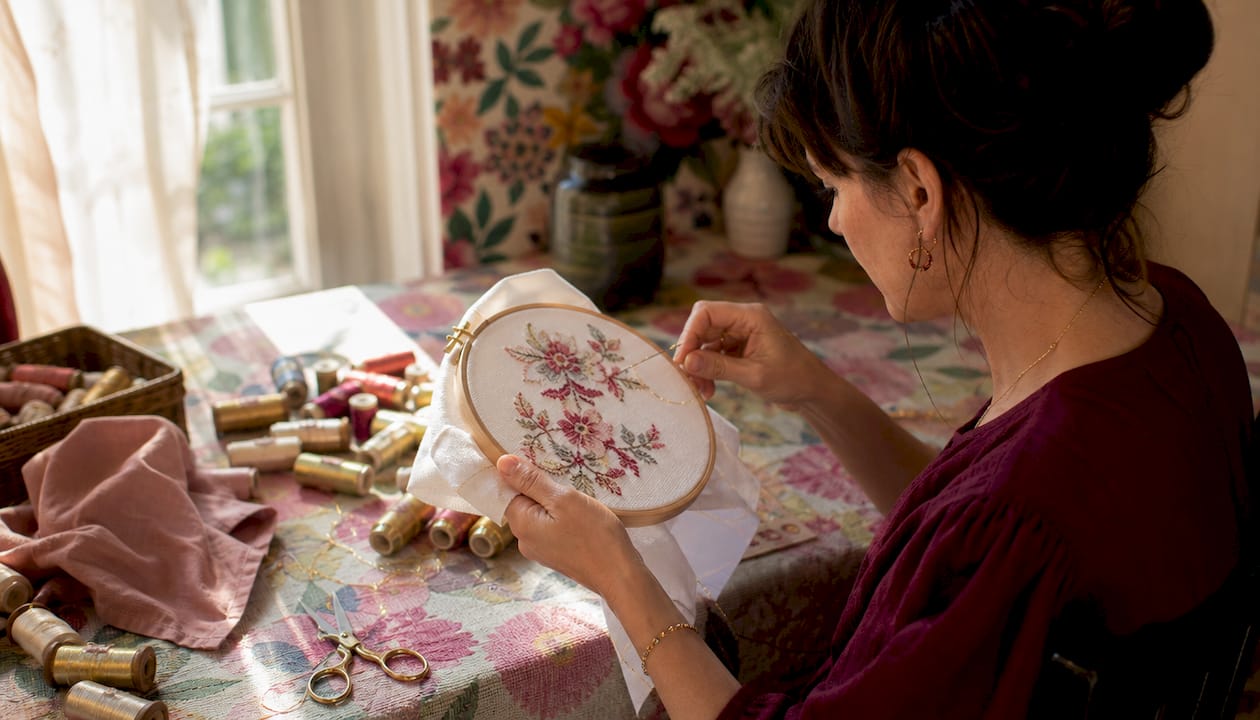 Person stitching metallic thread in cross stitch hoop