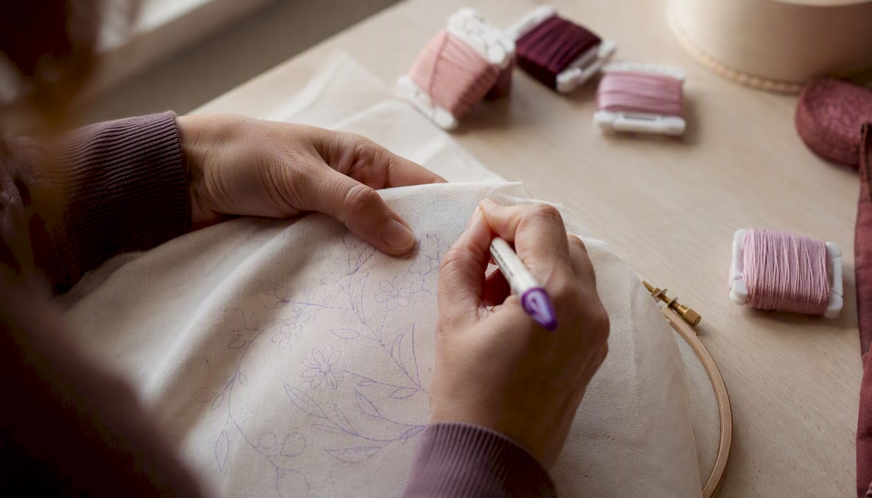 Hands re-tracing embroidery pattern on fabric