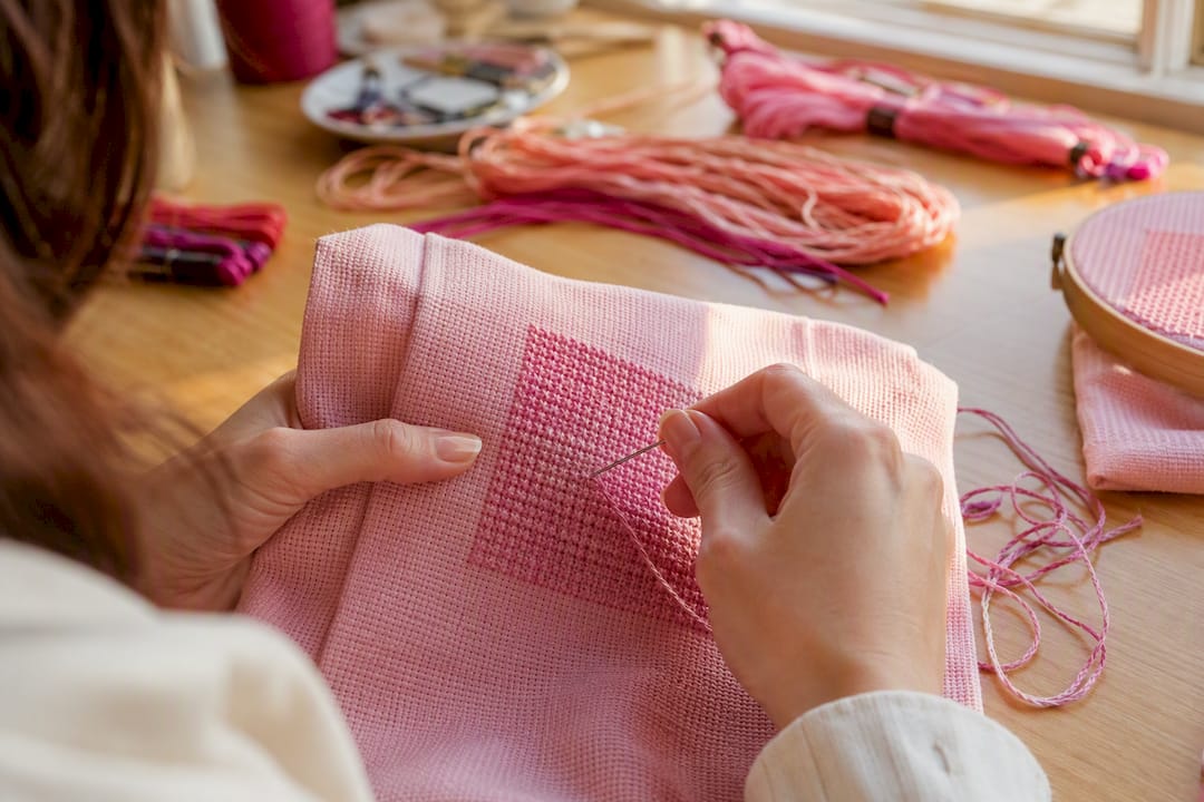 Hands stitching rows of cross stitch on fabric
