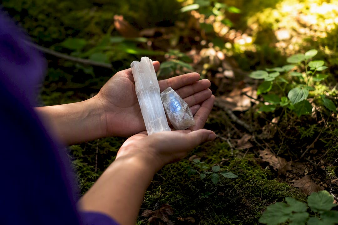 Hands holding selenite and moonstone crystals