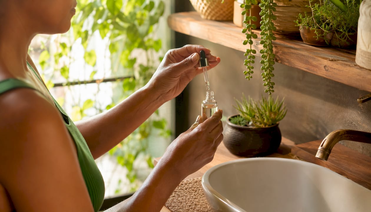 Hands holding copper peptide serum bottle over sink