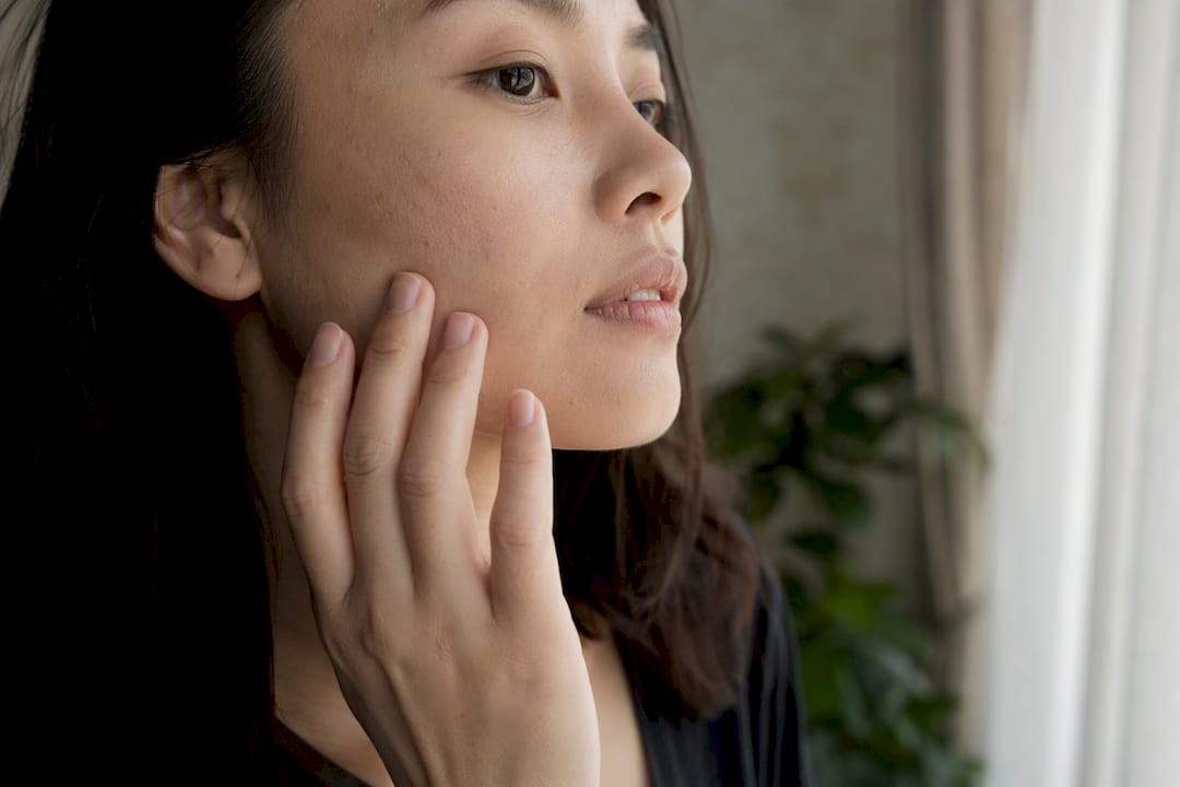 Person inspecting facial skin texture by window