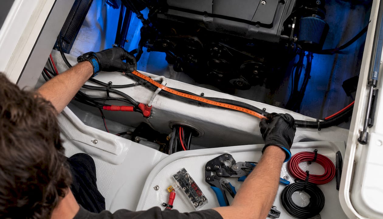 Hands measuring marine battery cable length on boat