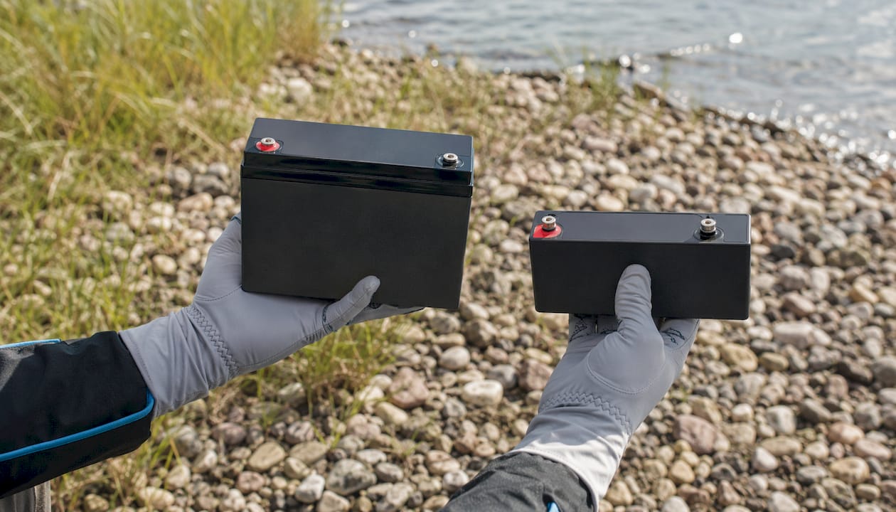 Hands comparing two marine battery types outdoors