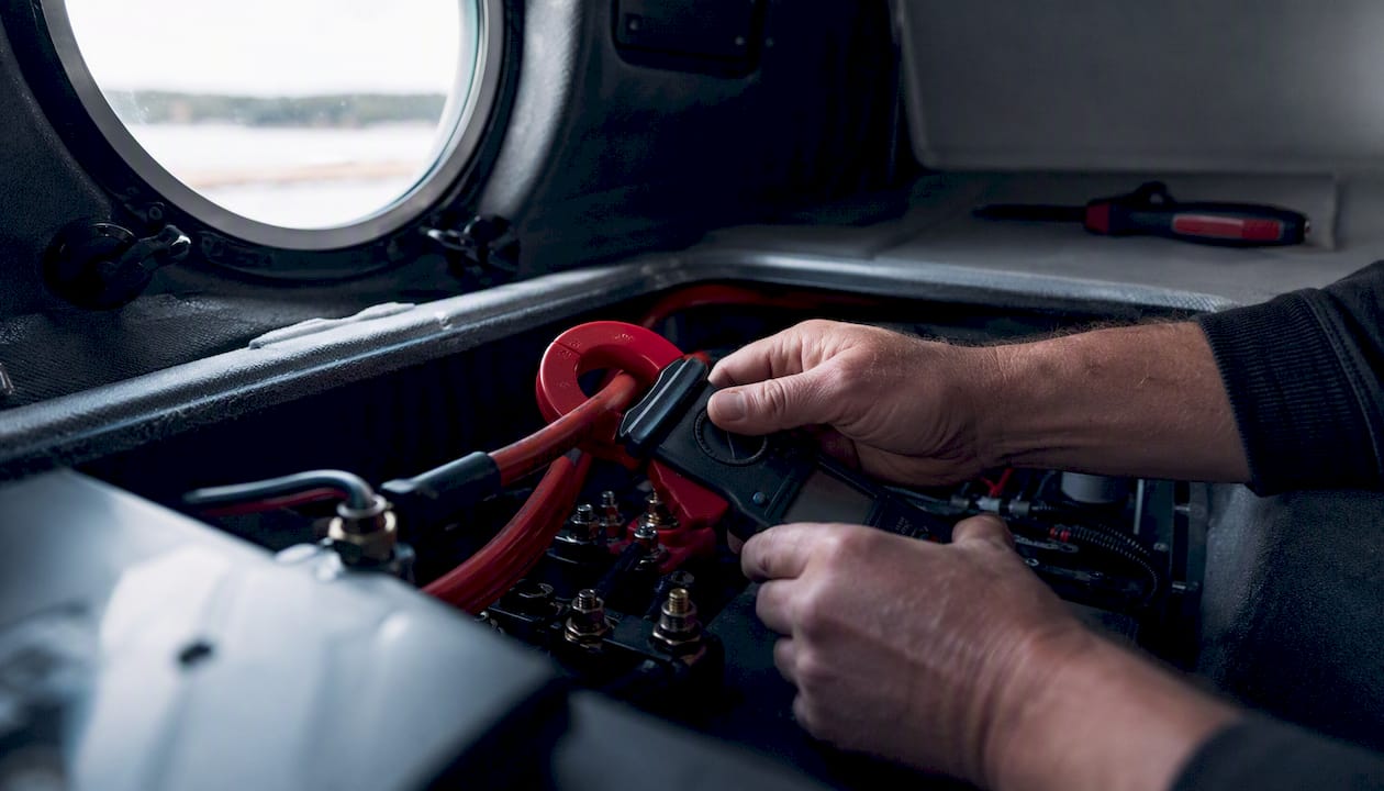 Hands measuring current draw with ammeter clamp