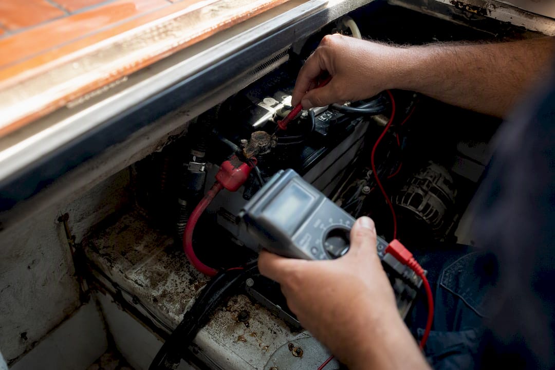 Hands testing battery voltage in vehicle engine bay