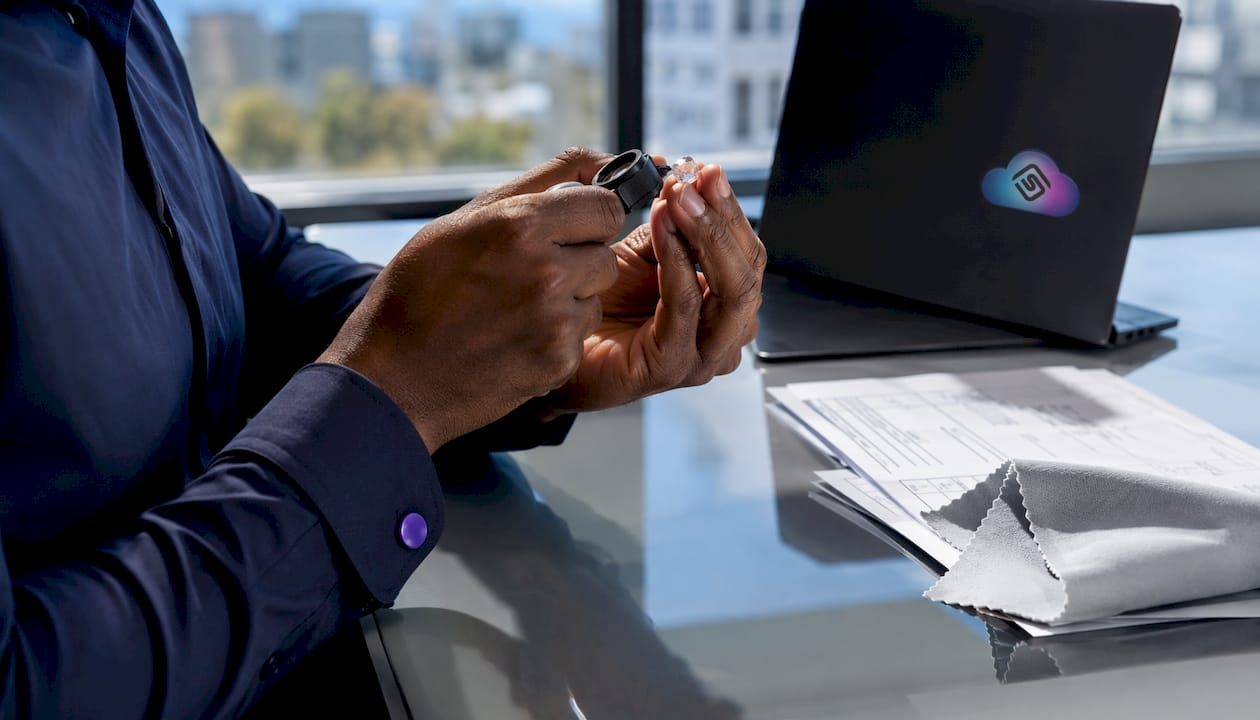Hands inspecting raw gemstone with jeweler’s loupe