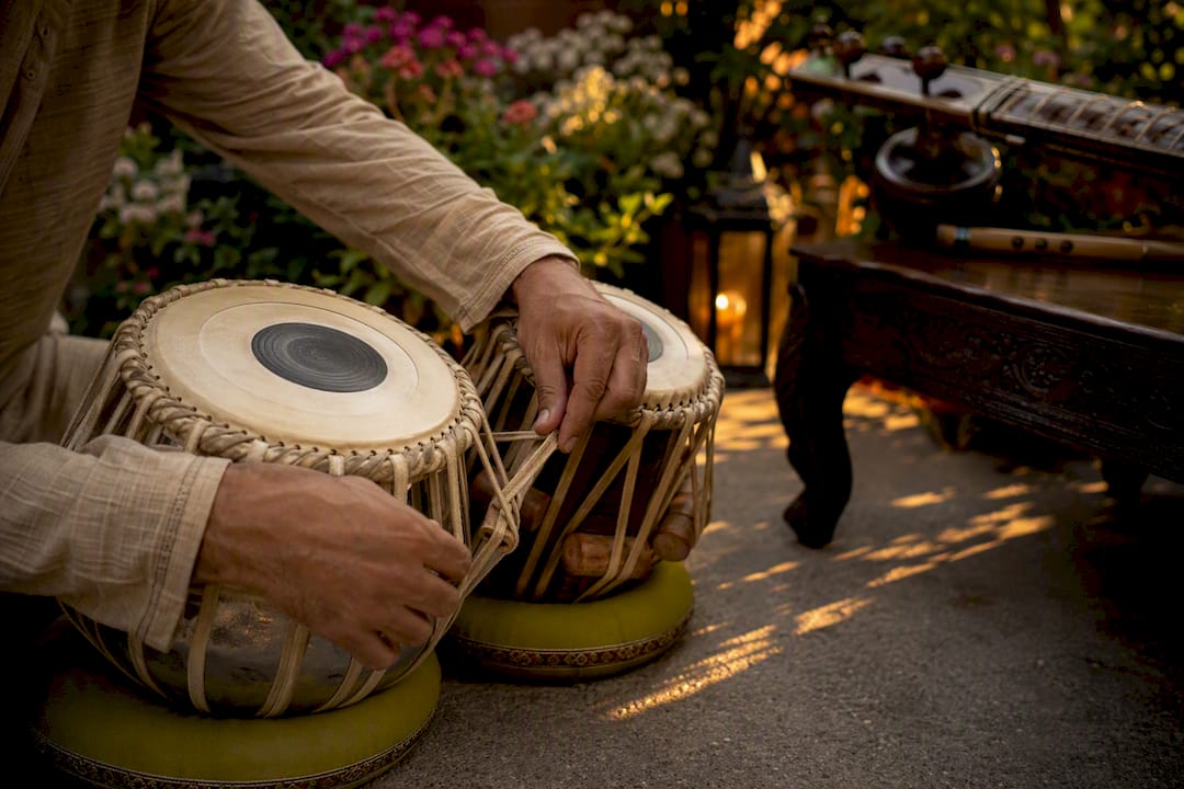 Hands tuning tabla beside sitar and flute