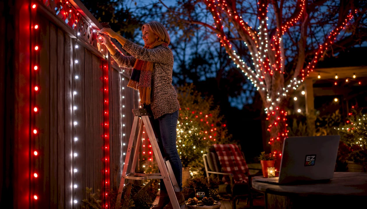 Woman installing modern holiday string lights on house