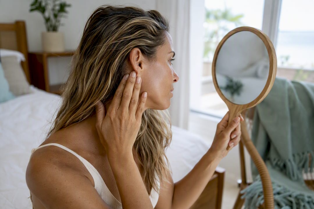 Woman checking ear and hairline in mirror